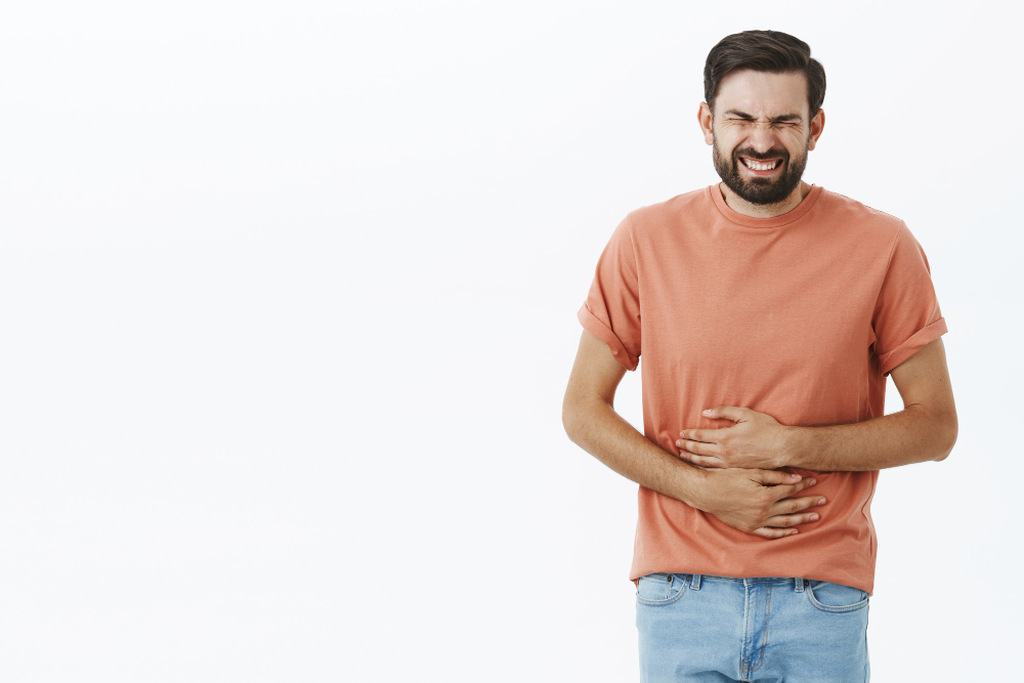 Homem com expressão de dor segurando o abdômen com as duas mãos, representando cólicas intestinais e a busca por como cortar a diarreia rapidamente.
