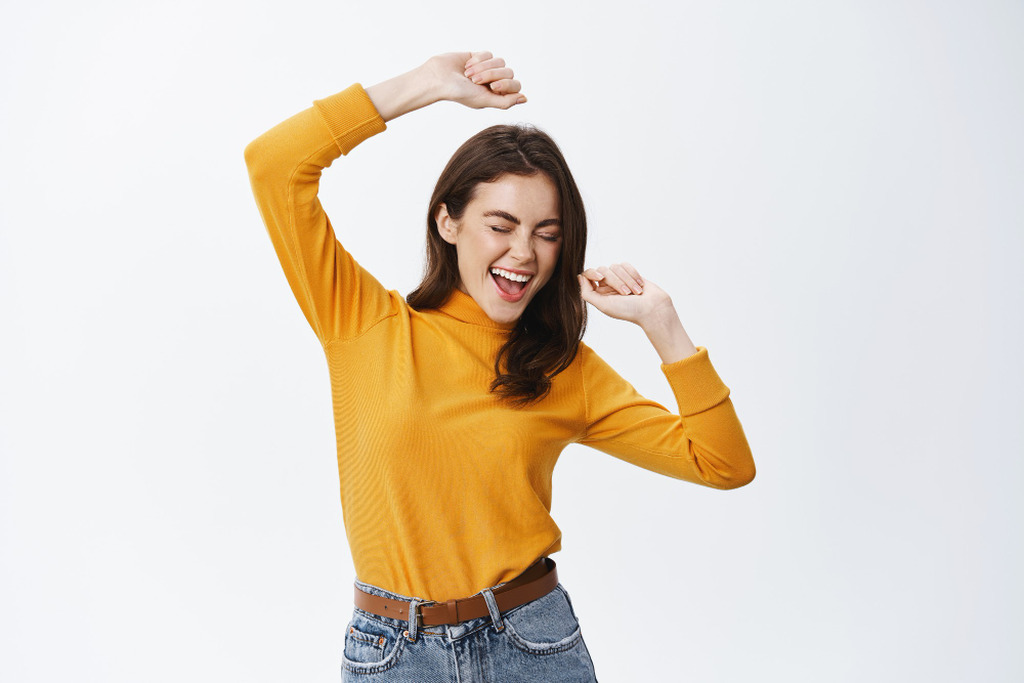 Mulher jovem e sorridente vestindo blusa amarela, com os braços levantados e os olhos fechados em um gesto de alívio e comemoração. A imagem ilustra a sensação de bem-estar e recuperação após aplicar os cuidados corretos de como tratar a diarreia.
