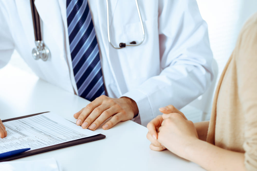 Paciente em consulta com um médico de jaleco branco para discutir resultados de exames e possíveis causas de muco gelatinoso nas fezes.