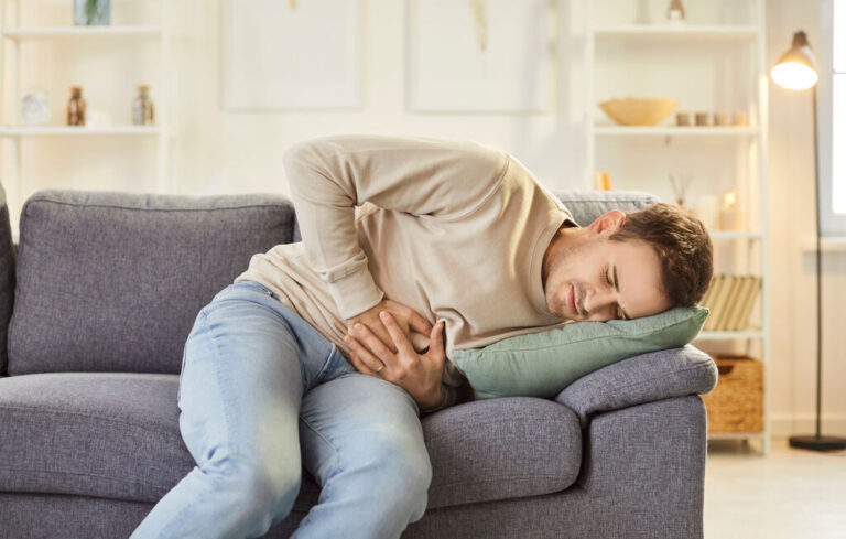 homem deitado no sofa com mao e dor na barriga