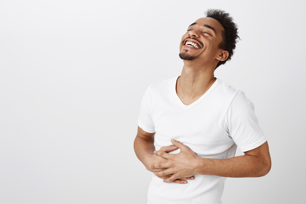 Homem sorri enquanto segura o abdômen, representando saúde intestinal e equilíbrio da flora intestinal.